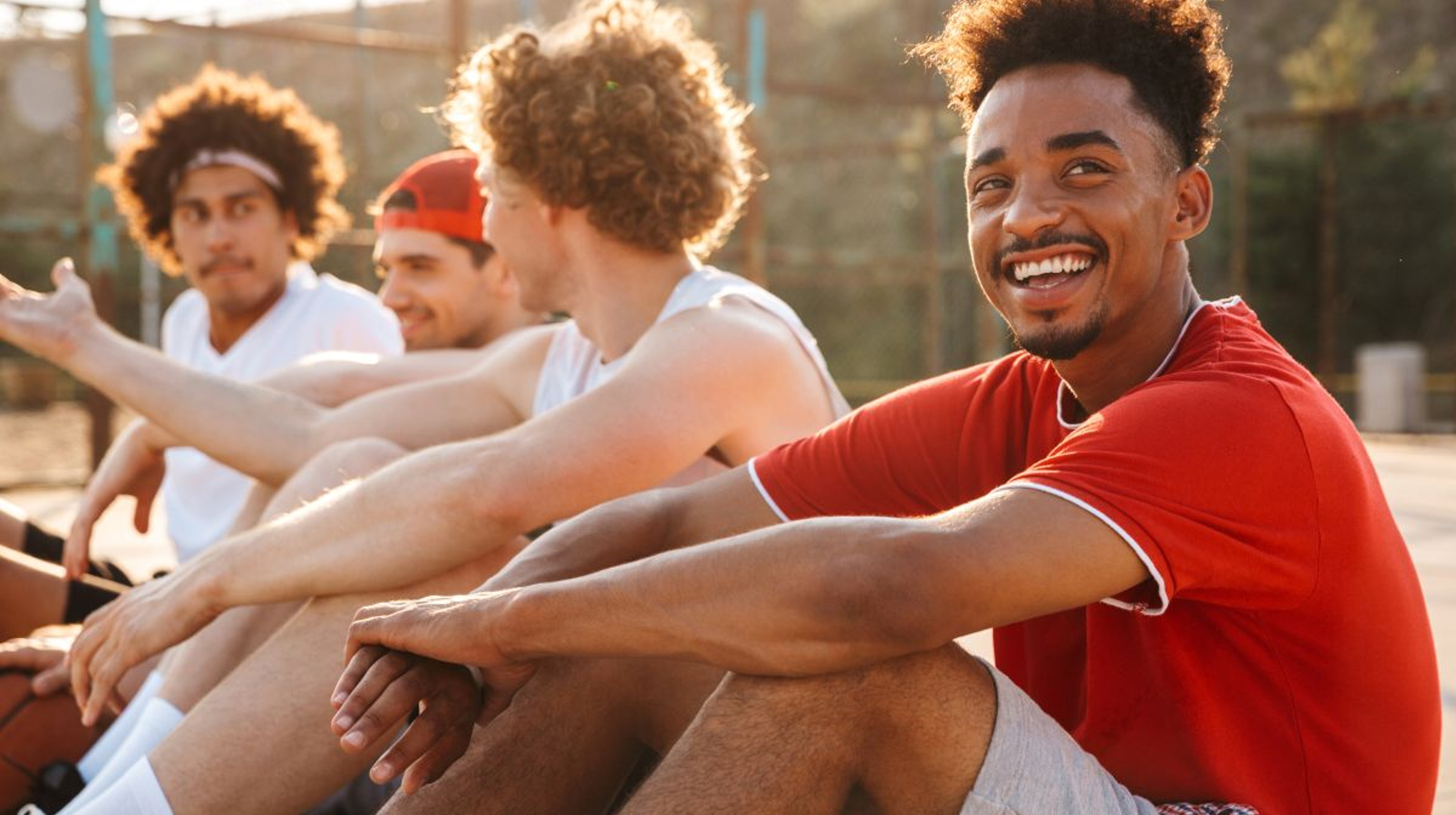 A group of young men sitting in a park, in the foreground, a Black man smiling