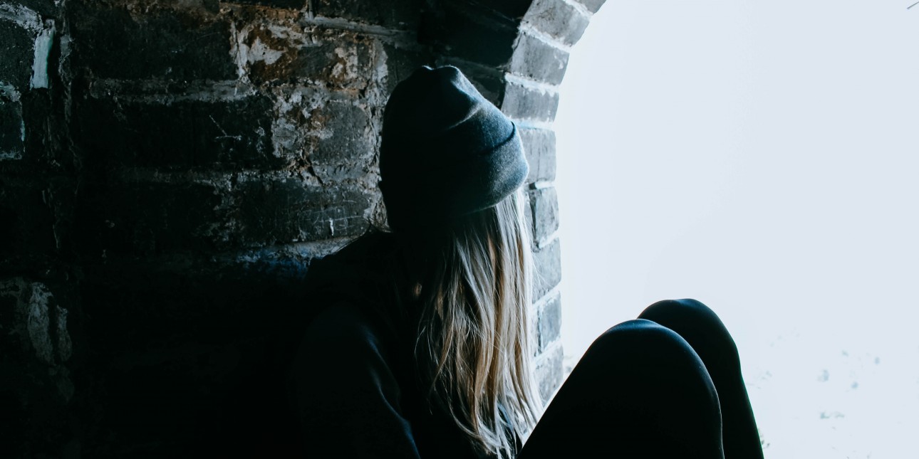 Woman sitting next to stone wall looking out window