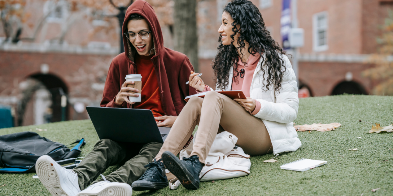 two young people sitting and collaborating with a laptop and notebook