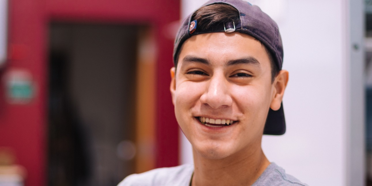 young Latinx person smiling and wearing a backwards baseball hat