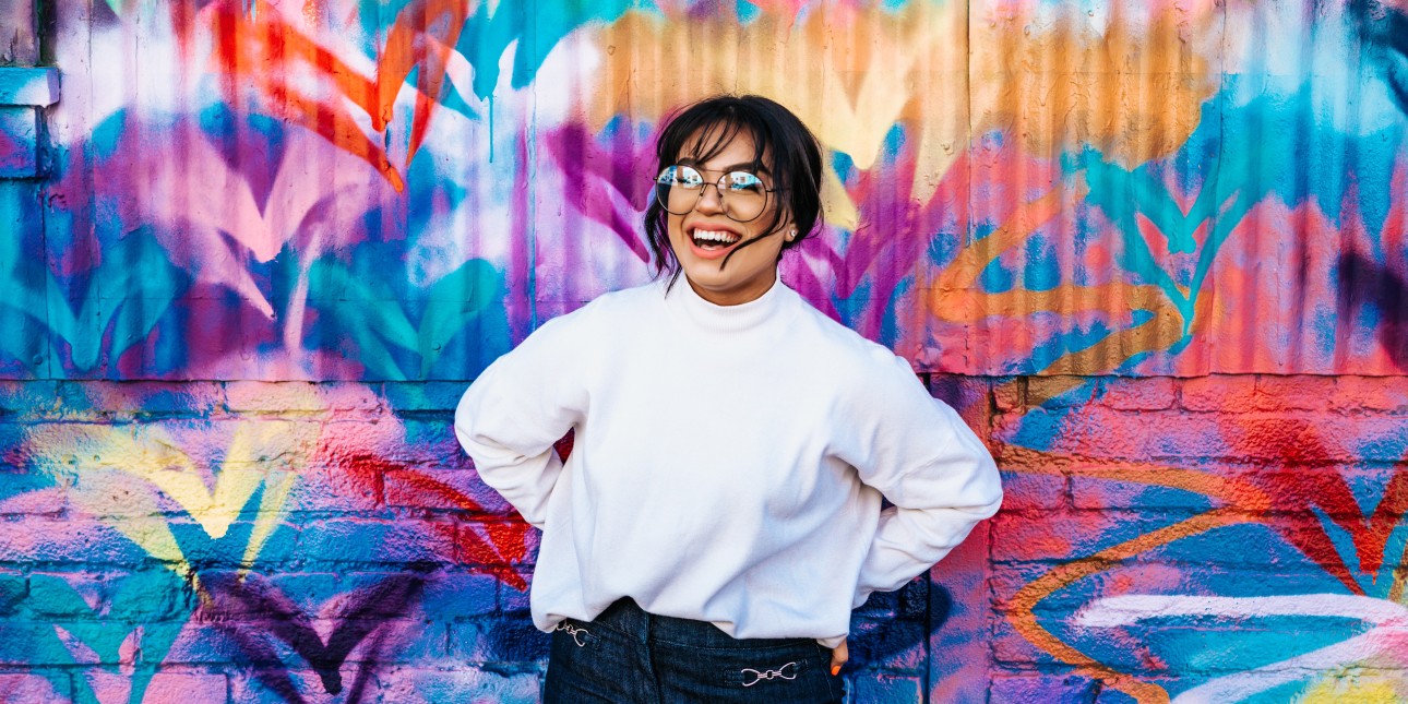 young person standing in front of a brightly colored spray painted wall