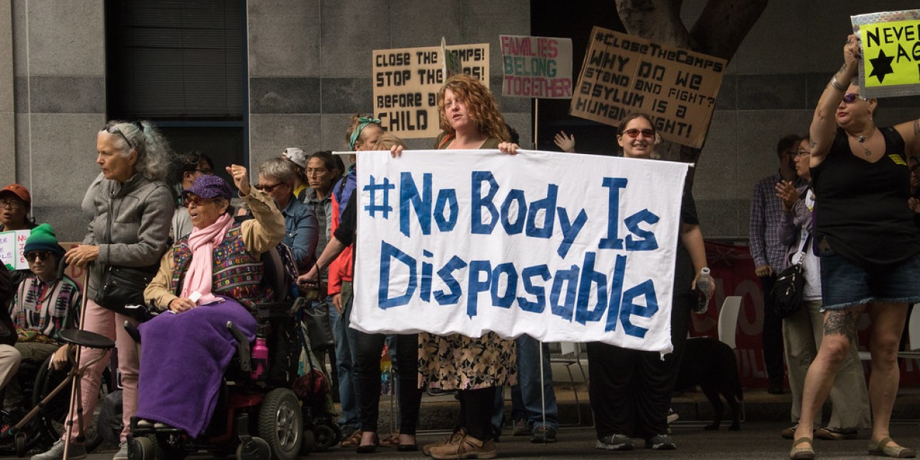 group of protesters - one holding a sign reading "#No Body Is Disposable"