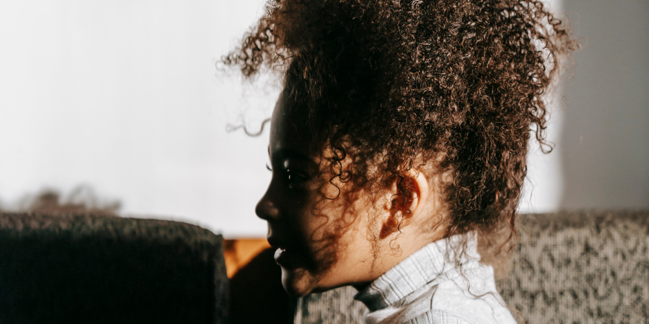 young Black girl in profile looking to the left with curly hair in on top of their head