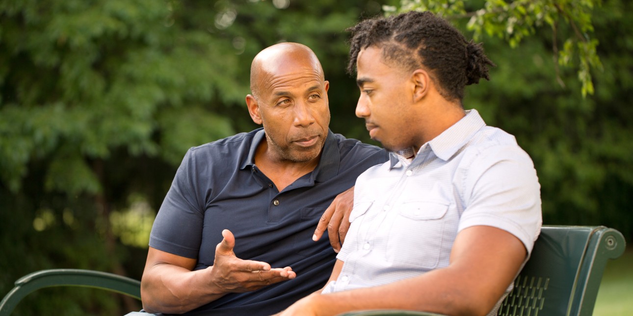 a young person and adult sitting on a park bench talking