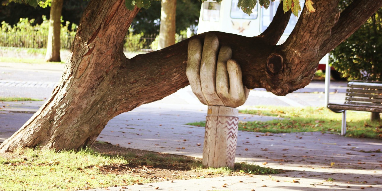 a carving of a hand holding up a tree branch in a park