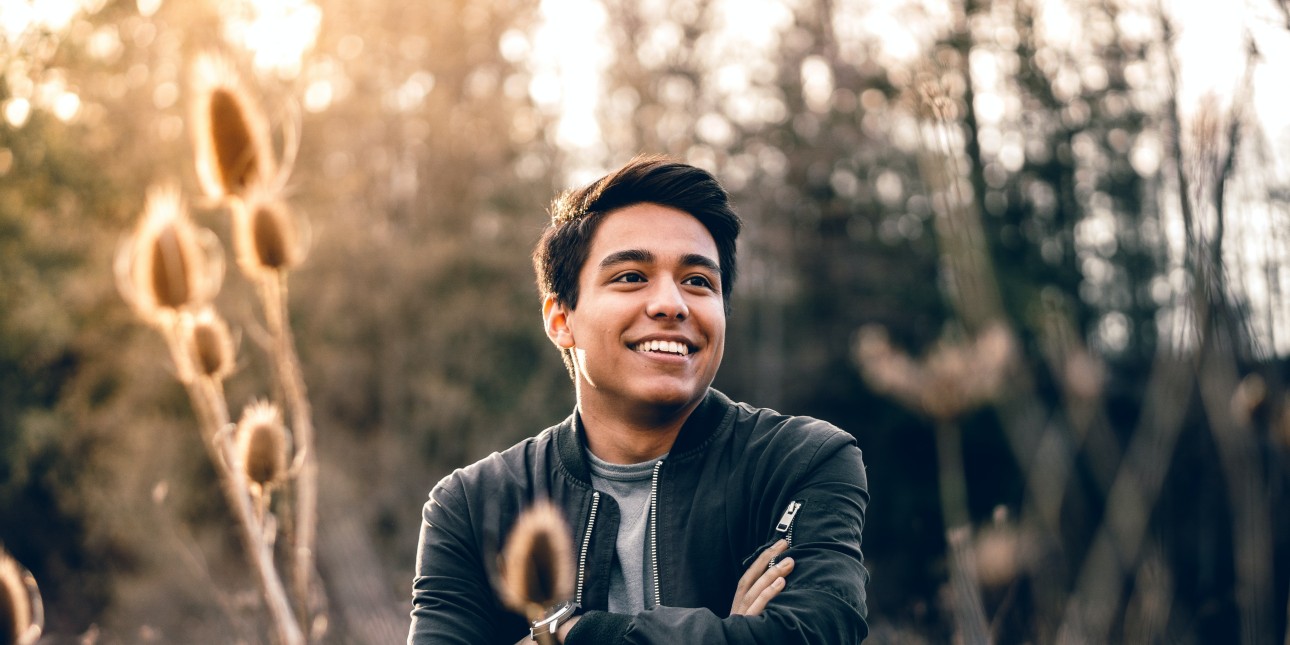 Image of a smiling man, with arms crossed, in the middle of a field. 