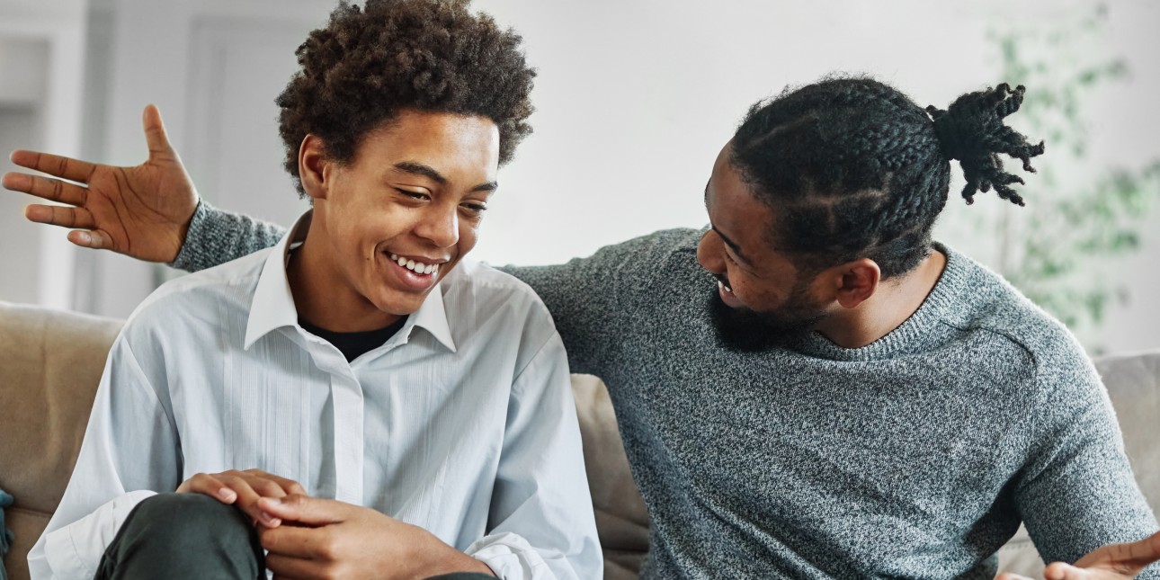 young and older black man smiling, talking, and sitting on a couch