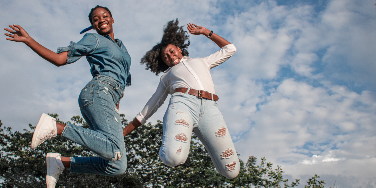 two Black girls smiling and jumping in the air