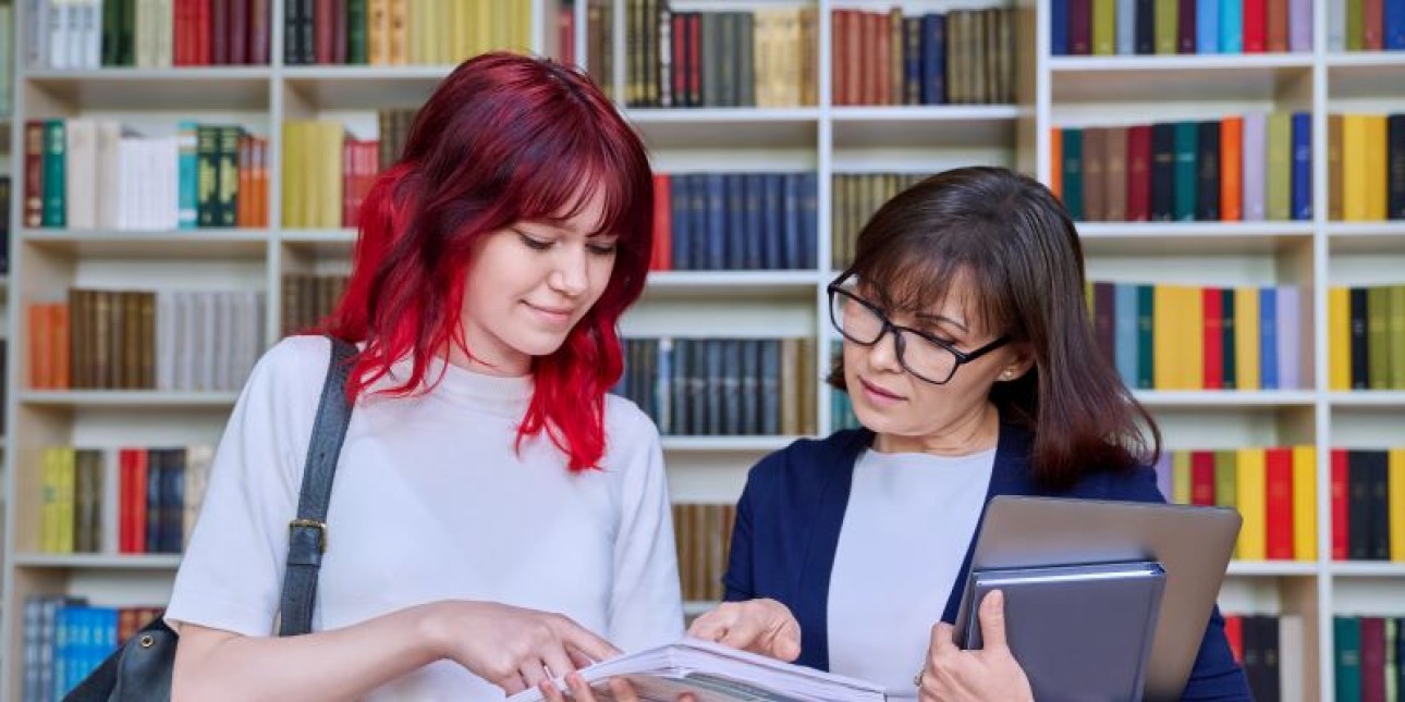 a young person with red hair and an adult wearing glasses in a library