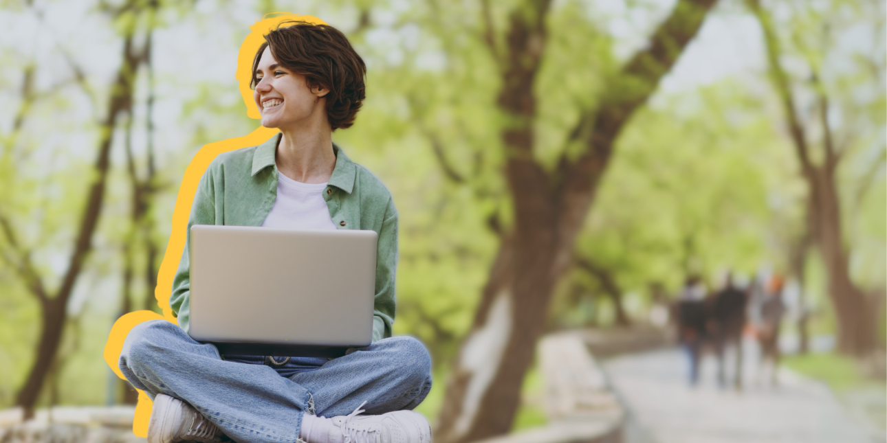 A young woman sitting outside on a bench with her laptop
