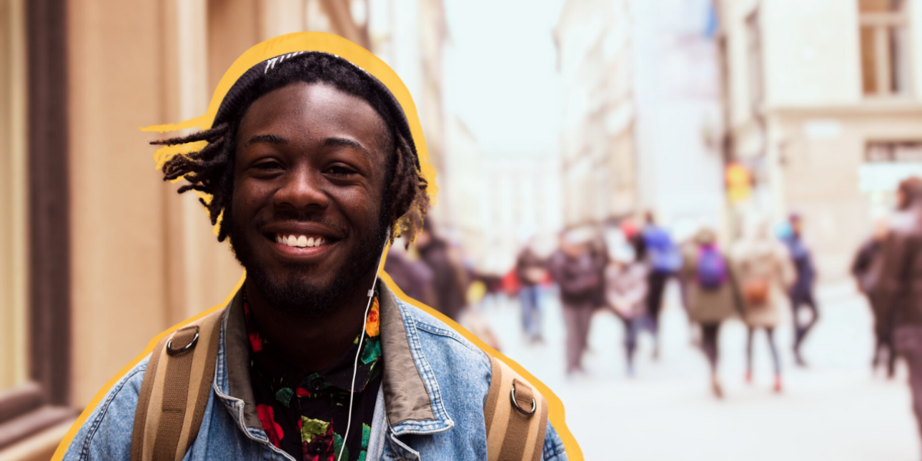 A young smiling person wearing a backpack in focus, a city street with pedestrians in the background