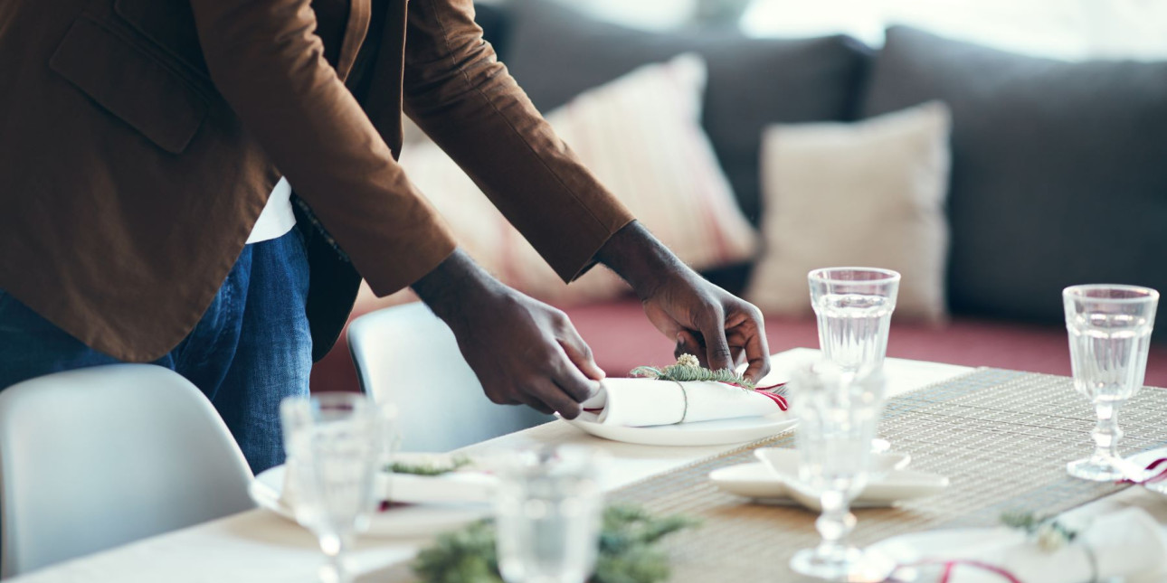 A Black man places a plate at a dining table