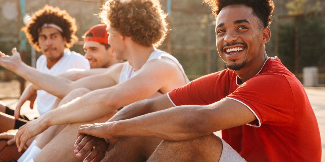 A group of young men sitting in a park, in the foreground, a Black man smiling