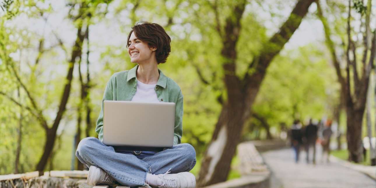 A young woman sitting outside on a bench with her laptop