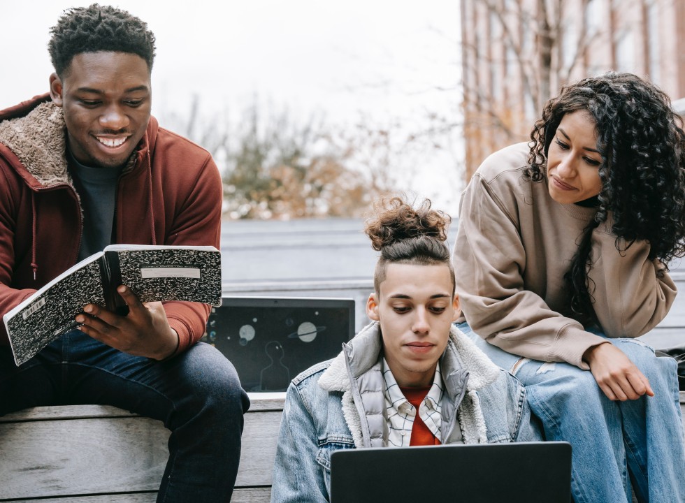 three young adults sitting with a notebook and laptop