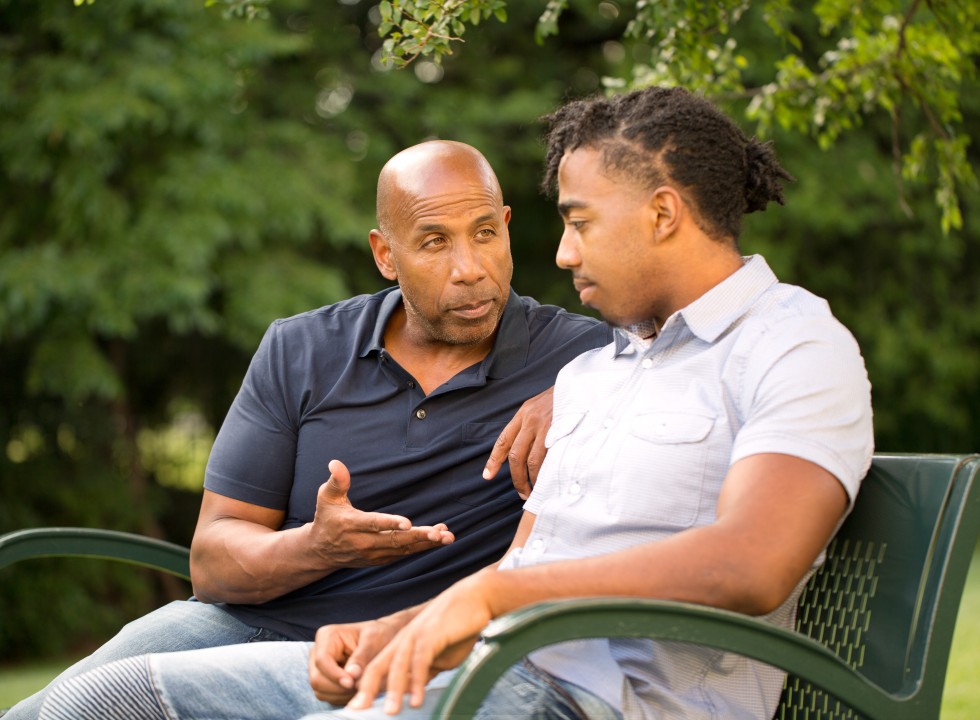 young person and adult sitting on a park bench talking