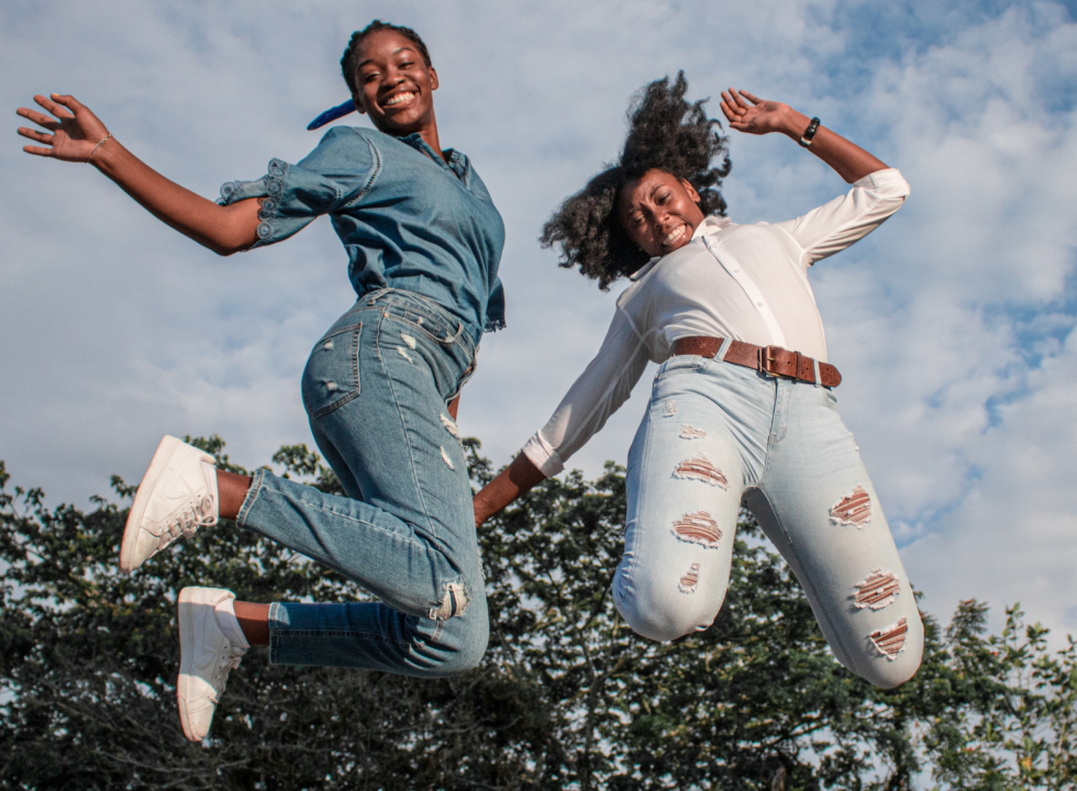 two Black girls smiling and jumping in the air
