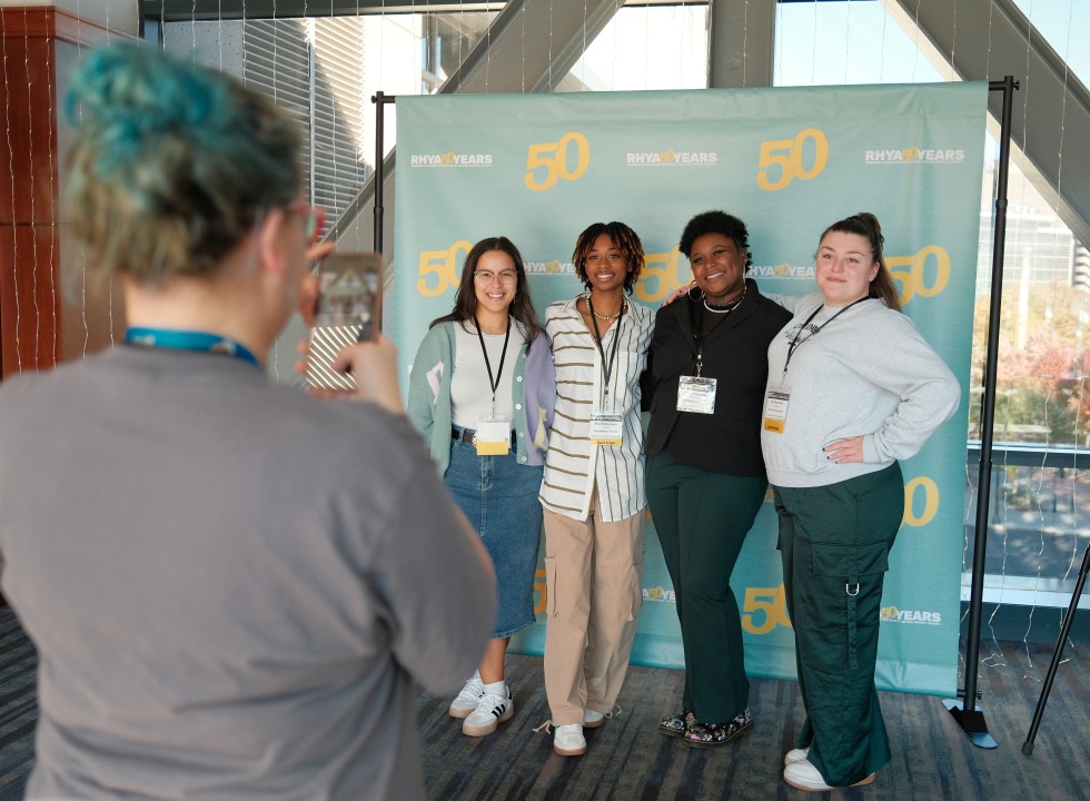 A group of people have their photo taken in front of an event backdrop.