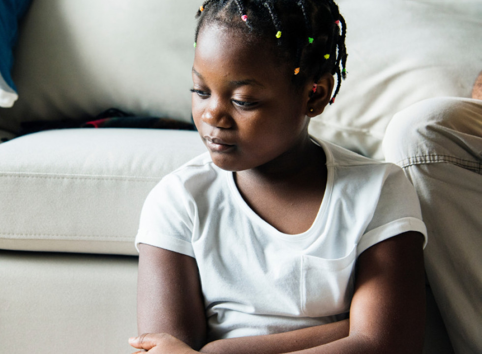 A young girls sitting next to a couch by herself