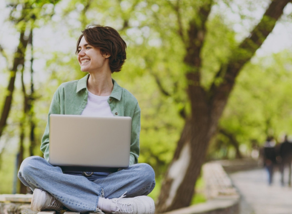Young person sitting outside in a park with a laptop 