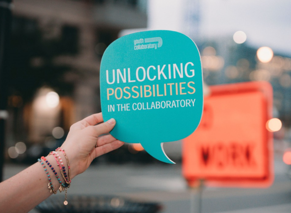 A hand holding a speech bubble that reads "Unlocking Possibilities in the Collaboratory"