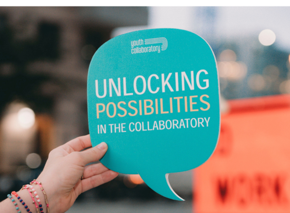 Hand holding a speech bubble sign that reads "Unlocking Possibilities in the Collaboratory"
