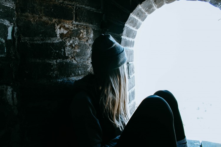 Woman sitting next to stone wall looking out window