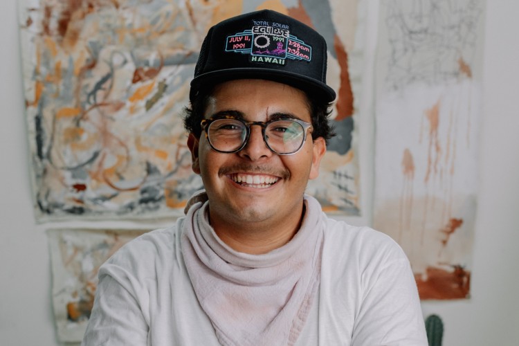 young person standing with a hat on and arms crossed, smiling