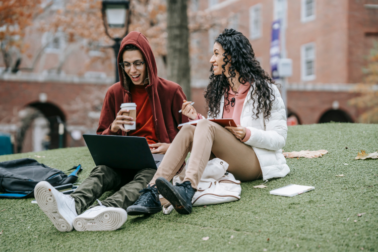 two young people sitting and collaborating with a laptop and notebook