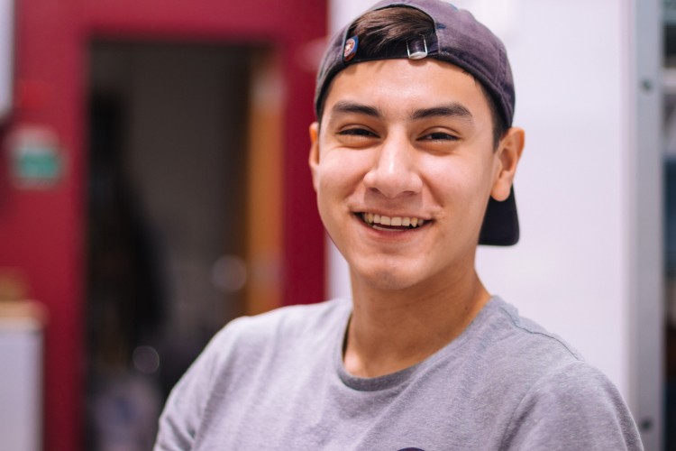young Latinx person smiling and wearing a backwards baseball hat