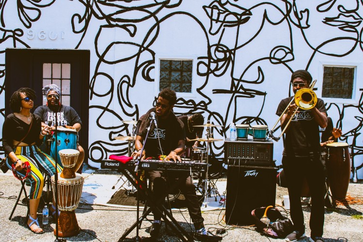 6 Black musicians play music in front of a mural outside