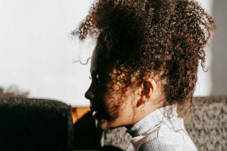 young Black girl in profile looking to the left with curly hair in on top of their head