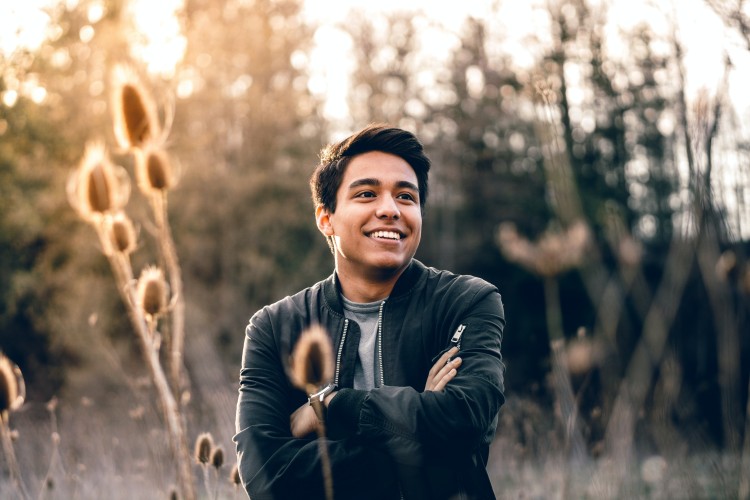 Image of a smiling man, with arms crossed, in the middle of a field. 