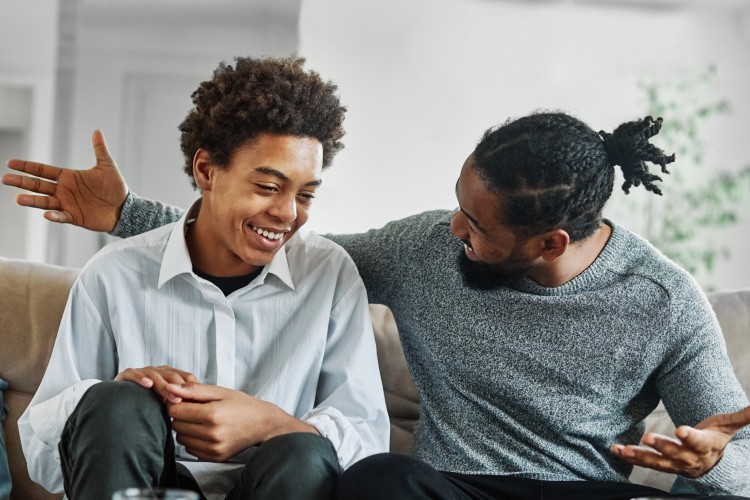 young and older black man smiling, talking, and sitting on a couch