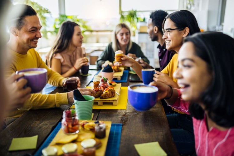 Happy group of multiracial friends having breakfast together and talking at coffee bar restaurant - United millennial people laughing and having fun while drinking hot coffee
