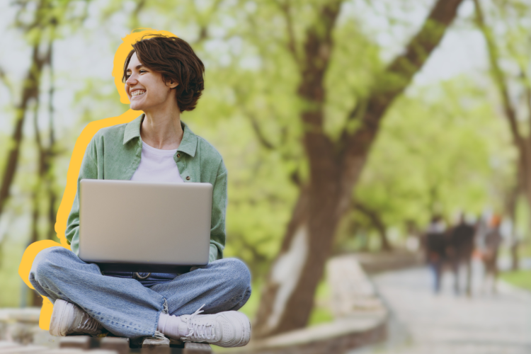 A young woman sitting outside on a bench with her laptop