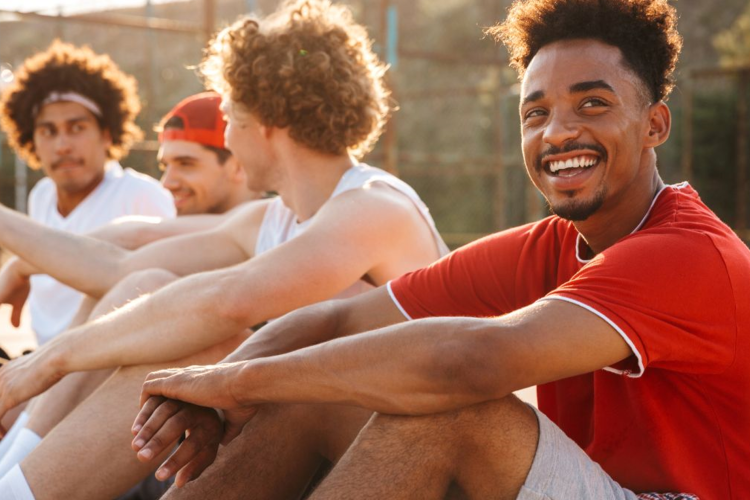 A group of young men sitting in a park, in the foreground, a Black man smiling