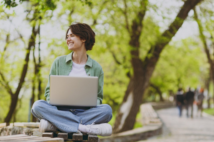 A young woman sitting outside on a bench with her laptop